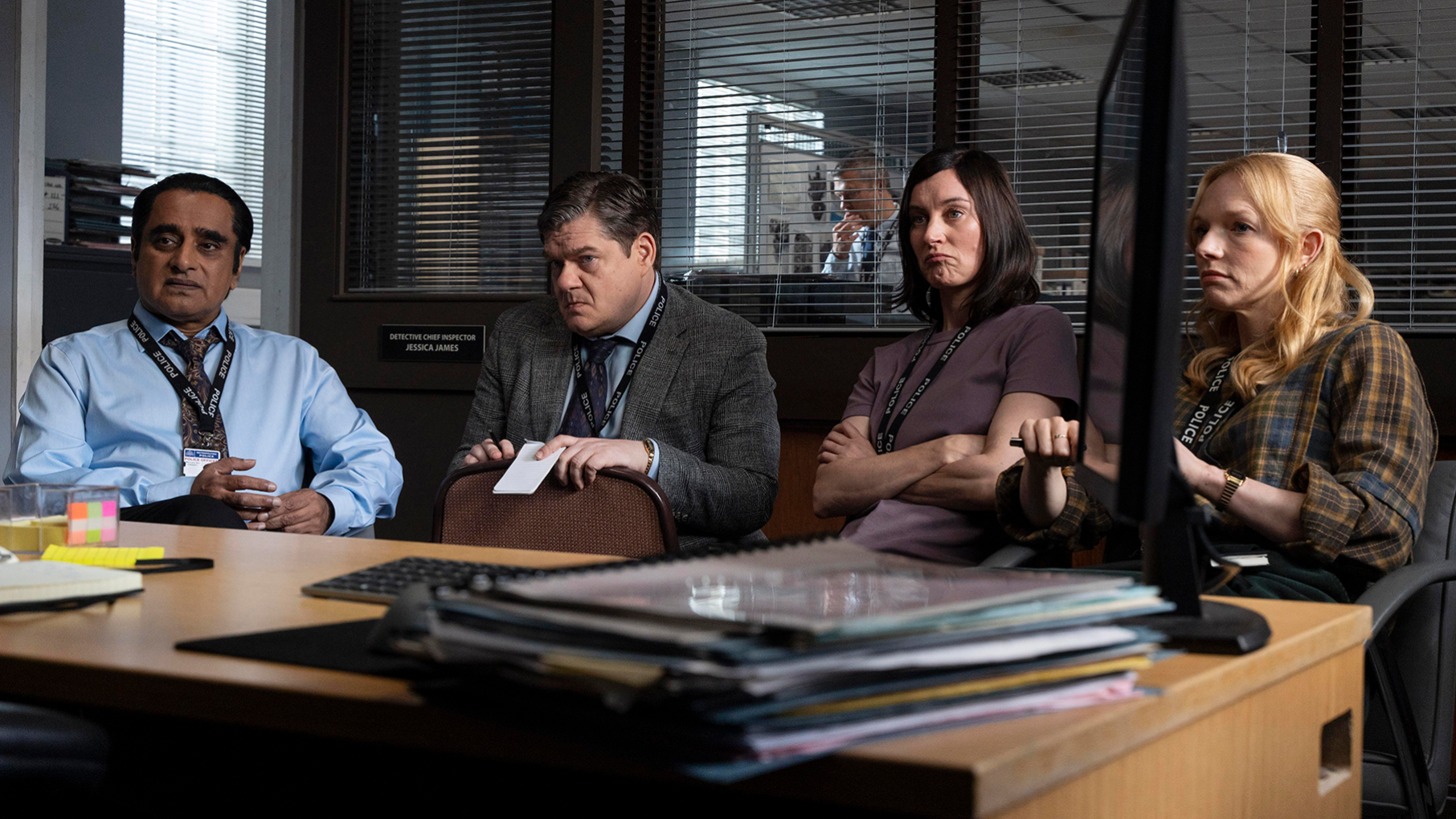 The team of detectives sits facing a desk